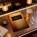 a menu for a happy hour event at a bar, with a glass of beer and a bowl of nuts on the counter.