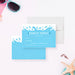 a blue invitation card with a water splash design, placed on a white background. There are sunglasses, a starfish, and some seashells in the background, suggesting a beach or ocean-themed setting.