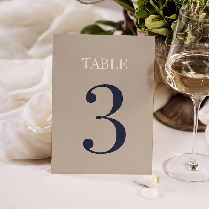 A table number 3 sign is placed on a table with a glass of wine and a potted plant in the background.