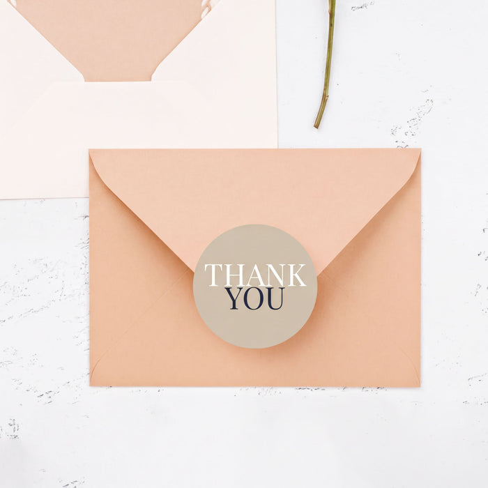 a peach-colored envelope with a round "Thank You" sticker on it, placed on a white surface.