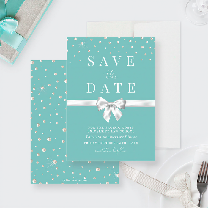 a teal-colored invitation card with a white ribbon and bow, along with a gift box and a fork on a white surface.