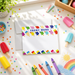 a variety of colorful items, including popsicle sticks, crayons, and a drawing of a rainbow, arranged on a white surface.