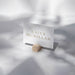 A white business card with the name "KAiley McMillan" printed on it, placed on a wooden stand against a blurred background.