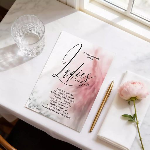 a table with a pink and white invitation card for a ladies lunch event, a glass of water, a pen, and a pink flower.