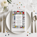 a dinner party invitation card with a geometric design, placed on a white tablecloth with silverware and a vase of flowers.