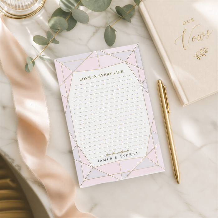 a marble table with a pink and white geometric paper pad, a gold pen, and a gold notebook with the text "Our Vows" written on it. There is also a green plant and a ribbon visible in the scene.