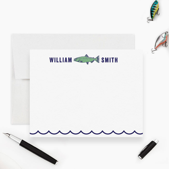 a personalized note card with a fish illustration, a pen, and a pair of fishing lures, all arranged on a white background.