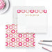 a white envelope with a pattern of pink and white donuts, along with a note card with a similar pattern. There are also some pens and a plate of pink frosted donuts in the background.