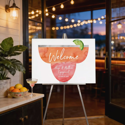 a welcome sign with a cocktail glass and a cocktail umbrella, placed on a stand in a room with string lights and a potted plant.