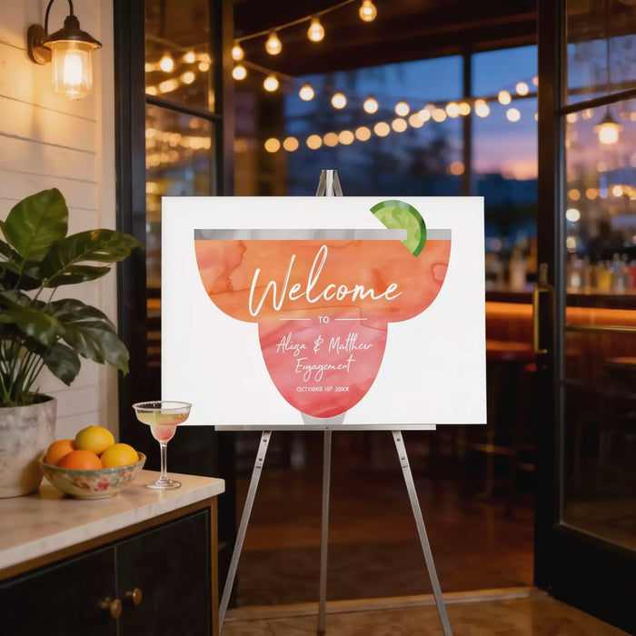 a welcome sign with a cocktail glass and a cocktail umbrella, placed on a stand in a room with string lights and a potted plant.