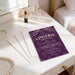 a purple invitation card for a lingerie shower, placed on a white dresser next to a mirror and some pearls.