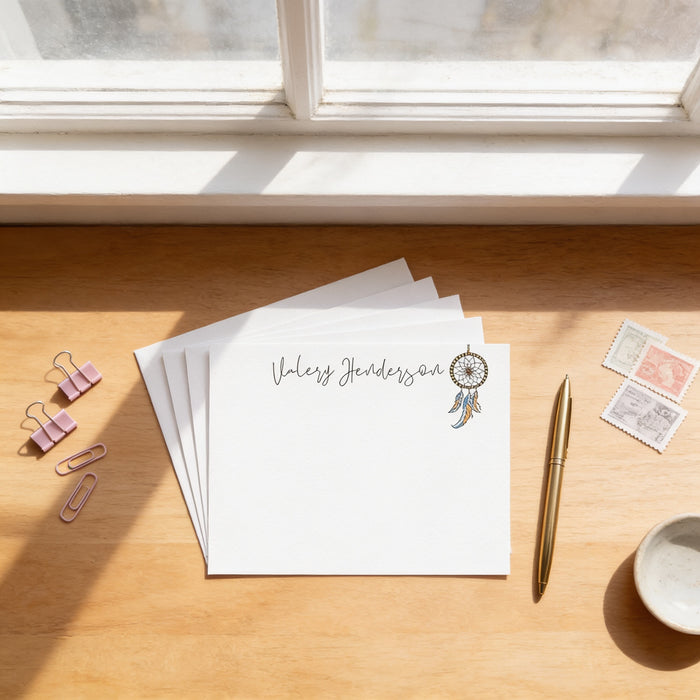 a desk with a stack of white envelopes, a pen, a gold pen, a bowl, and some postcards.