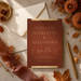 a wedding invitation for a couple named "SCARLEETTE & ALEJANDRO" with details about the wedding celebration, including the date, time, location, and dress code. The invitation is surrounded by autumn-themed decorations, such as leaves, flowers, and a pen, creating a warm and inviting atmosphere.