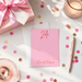 a pink card with the number "21" and the name "Daria" written on it, surrounded by pink confetti, a pink pen, and a pink gift box with a pink ribbon.