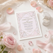 a wedding invitation card with a pink and white color scheme, surrounded by various wedding-related items such as a ring box, rose petals, and gemstones.
