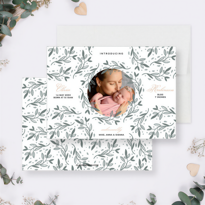 The image is a white card with a floral pattern and a photo of a woman holding a baby. The card is surrounded by greenery and small white flowers, creating a natural and serene atmosphere.