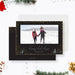 Modern black holiday photo card featuring gold confetti accents, a wide photo frame, scripted Happy Holidays greeting, and small illustrated winter trees.