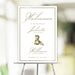Elegant wedding welcome sign with gold border, floral ampersand, and personalized names, displayed on an easel for entrance decor.