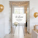 a white sign with gold lettering welcoming guests to Laura Mahoney's birthday celebration. The sign is displayed in a hallway with a floral arrangement on the floor in front of it. The hallway is decorated with gold balloons, and there is a table with a gift box on it.