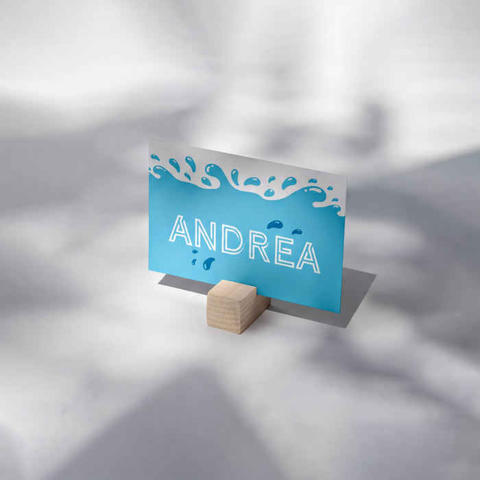 A blue card with the name 'ANDREA' written on it, placed on a wooden stand.