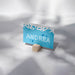 A blue card with the name 'ANDREA' written on it, placed on a wooden stand.