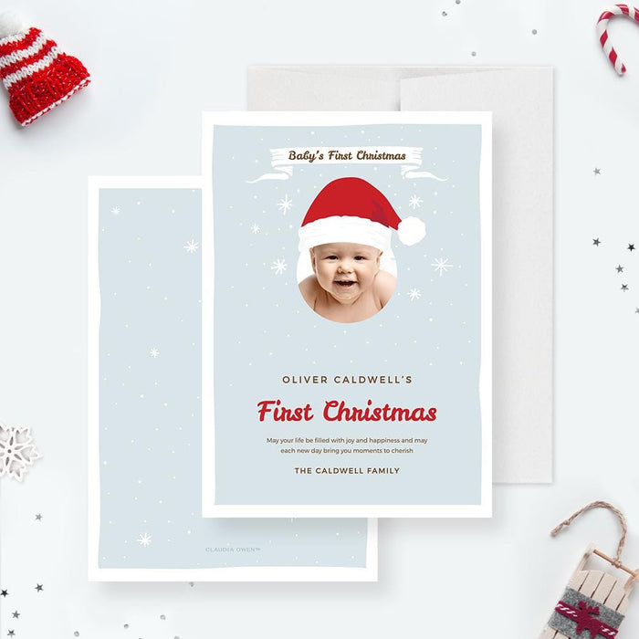 Baby’s first Christmas card featuring a cute baby photo framed with a Santa hat, light blue snowy background, and red festive text.