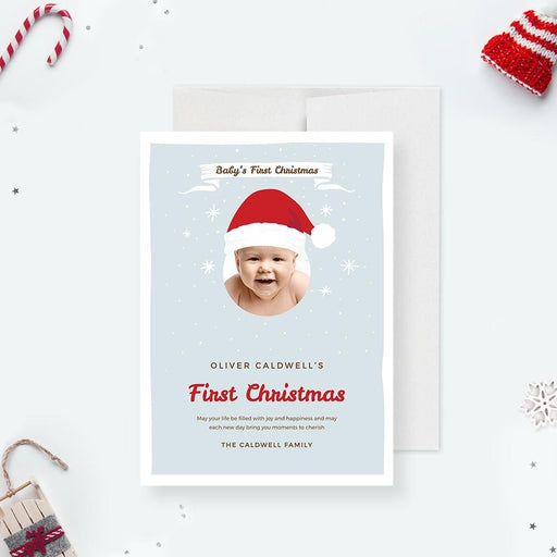 Baby’s first Christmas card featuring a cute baby photo framed with a Santa hat, light blue snowy background, and red festive text.