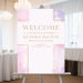 Pink watercolor baptism welcome sign for a christening celebration displayed on an easel at a religious event.