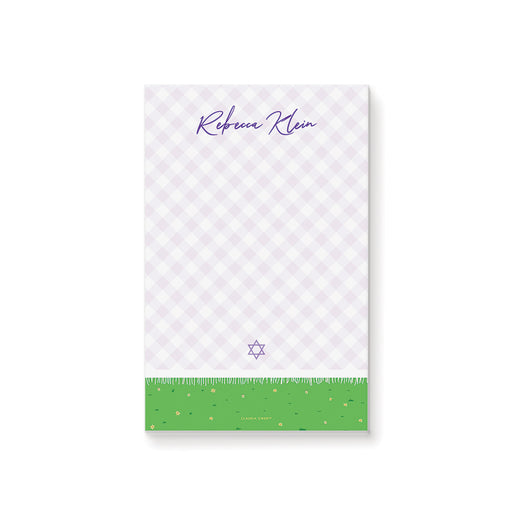 Personalized bat mitzvah notepad with a lavender picnic blanket, purple script name, and a green grass border with flowers
