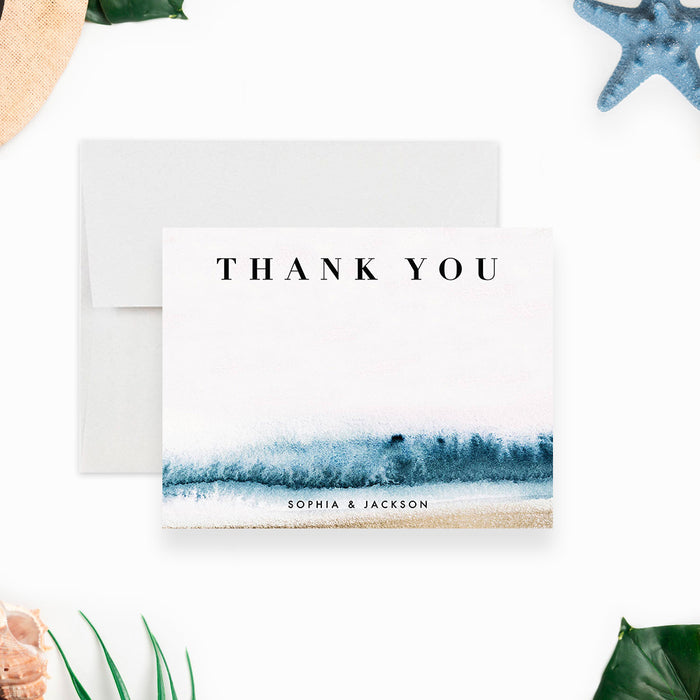 beach wedding thank you card with blue ocean wave artwork, sand-toned accents, couple names, and coastal design-front