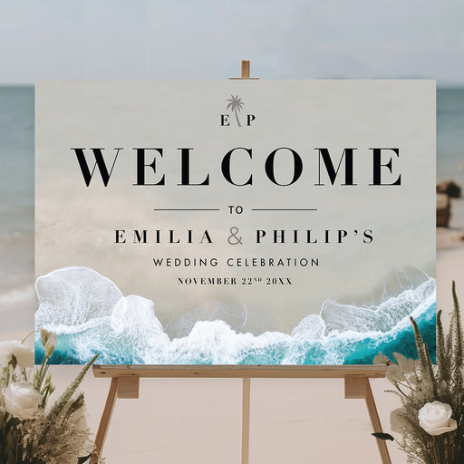 Personalized beach wedding welcome sign featuring ocean waves and modern black text, displayed on an easel at a coastal ceremony.