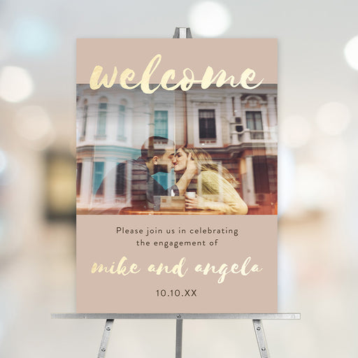 Personalized engagement welcome sign featuring a couple photo, beige and gold design, custom names, and event details displayed on an easel.