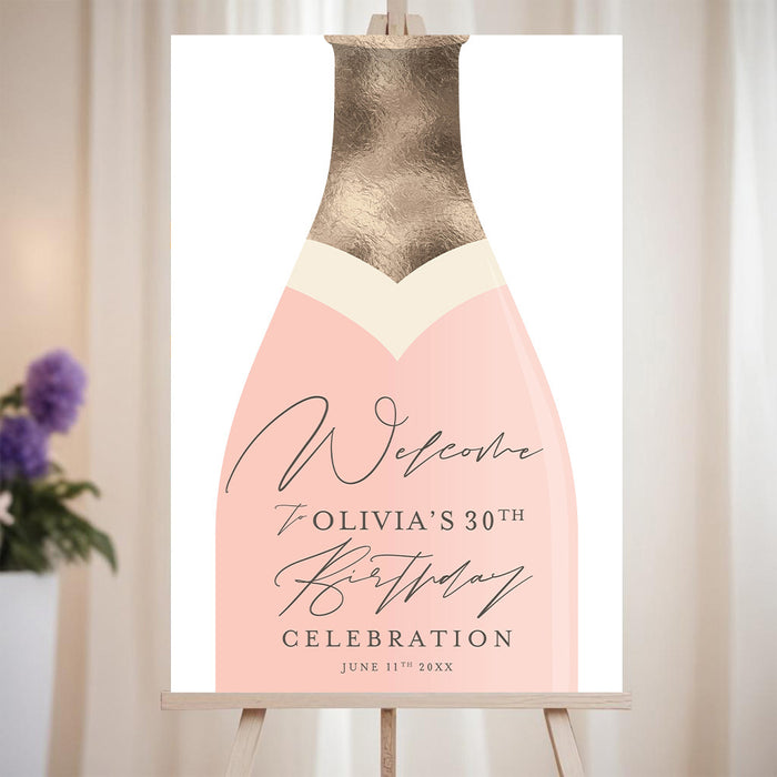 Blush pink champagne bottle welcome sign personalized for a birthday celebration, displayed on an easel for party décor.