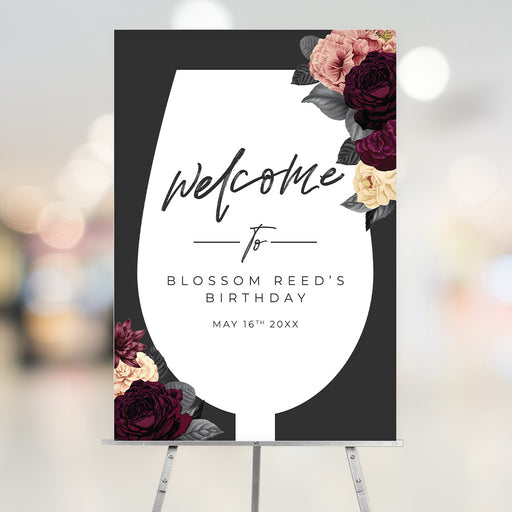 Wine glass–shaped birthday welcome sign featuring burgundy, blush, and cream florals on a black background with personalized text.