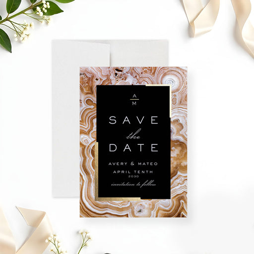 Geode wedding save the date card featuring a black center panel framed by a gold agate pattern in a modern elegant design-front