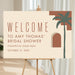 Boho bridal shower welcome sign with terracotta lettering, abstract desert arches, green palm tree, honoree’s name and event date