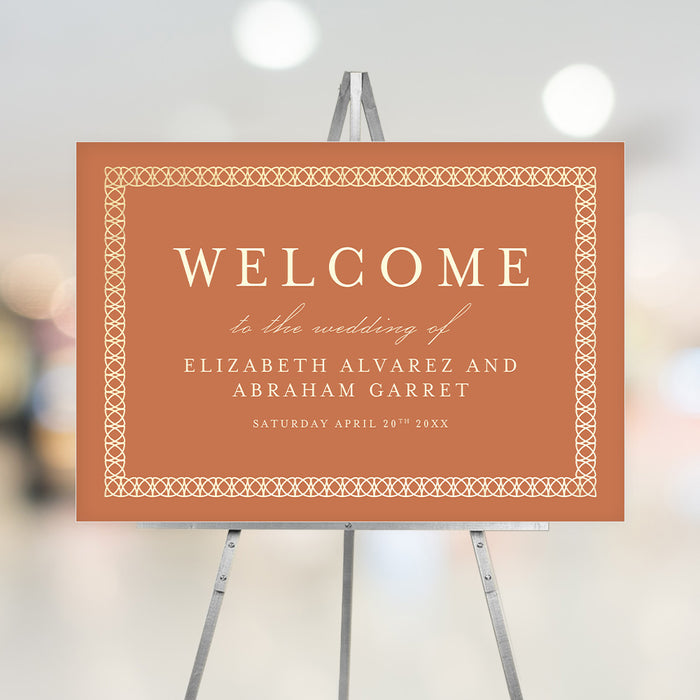Burnt orange wedding welcome sign featuring an intricate border design with customizable names and date, displayed on an easel.