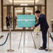 A man in a suit is placing a bouquet of white flowers on a marble pedestal in front of a sign that reads "Welcome Pacific Coast University Law School Thirties".