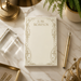 a desk with a white notepad with a gold frame, a gold pen, a gold lamp, a gold picture frame, and a gold star decoration.