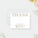 A white card with the text "THANK MILLA & MICHAEL YOU" printed on it, placed on a white background with some flowers and a ribbon visible in the background.