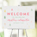 Custom Christmas welcome sign with festive holiday design, personalized with event details, displayed on an easel for party décor.