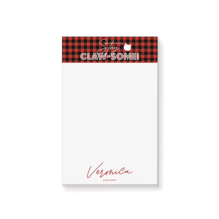 Notepad with red plaid border and text on a white background. The notepad reads Stay Claw-some!