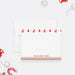 Personalized Christmas note card front with red reindeer, trees, green patterned borders and a family name, shown with a white envelope.