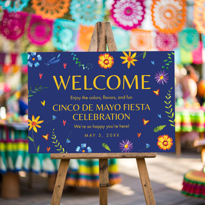 Cinco de Mayo welcome sign with colorful floral artwork, blue background, and fiesta party wording displayed on an easel