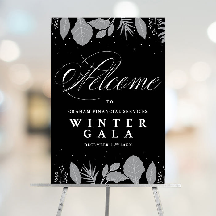 corporate winter gala welcome sign displayed on an easel with black background, gray botanical accents, elegant script lettering, and custom event details
