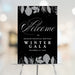 corporate winter gala welcome sign displayed on an easel with black background, gray botanical accents, elegant script lettering, and custom event details