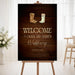 Rustic western wedding welcome sign with cowboy boots illustration on a dark wood background displayed on an easel.