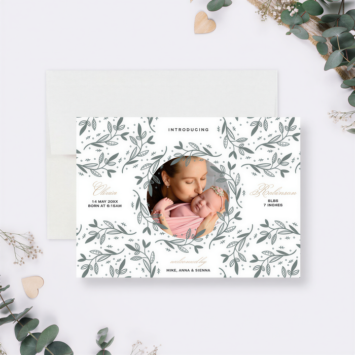 The image is a white card with a floral pattern and a photo of a woman holding a baby. The card is surrounded by greenery, and there is a heart-shaped object on the right side.