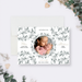 The image is a white card with a floral pattern and a photo of a woman holding a baby. The card is surrounded by greenery, and there is a heart-shaped object on the right side.