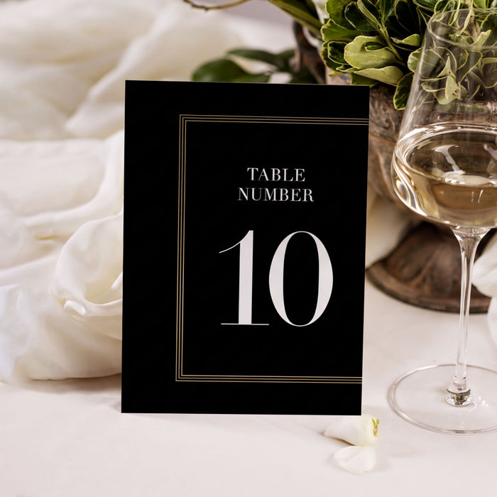 A black table number card with the number 10 displayed on it, placed on a table next to a glass of wine.